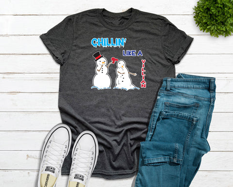 Adult dark heather grey tshirt with the graphic design of one snowman melting another snowman with a hair dryer and the saying "Chillin' Like A Villian". Designed and printed by Bare It Designs.