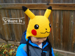 View from the front side of the Pokemon Pikachu character crochet toque with ear flaps and braided draw strings. Model is wearing size S toque. Handmade by Bare It Designs Ltd.