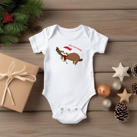 Christmas holiday themed white baby bodysuit. Graphic is a cute lazy sloth snoozing on a tree branch decorated with a string of lights with the saying Have a lazy holiday. Drawn in the kawaii art style by Bare It Designs. Designed and printed in Edmonton, AB, Canada.