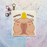 Peeker vinyl sticker/decal by Bare It Designs, Edmonton, AB, Canada. Peeker sticker featuring a capybara with its hands together in a prayer pose, with a small yellow duckling on top of its head doing the same pose and the words 'INNER PEACE' above it. 