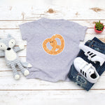 Light grey toddler / kid t-shirt with a cute classic pretzel twist drawing in the kawaii art style. Designed and printed by Bare It Designs.