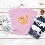 Light pink toddler / kid t-shirt with a cute classic pretzel twist drawing in the kawaii art style. Designed and printed by Bare It Designs.