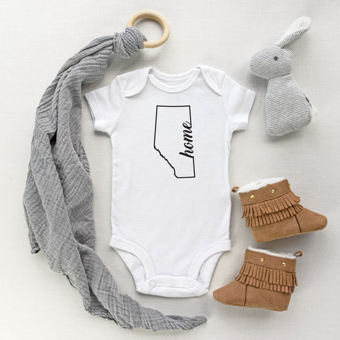 White baby bodysuit with the province of Alberta outline with the word home in script font designed and printed by Bare It Designs Ltd.