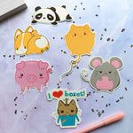 Various animal (panda, corgi, cat, pig, and mouse) vinyl stickers in the kawaii art style drawn and printed by Bare It Designs.