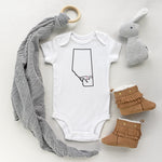 White baby bodysuit with the province of Alberta and a dinosaur outline with the heart of Drumheller designed and printed by Bare It Designs Ltd.
