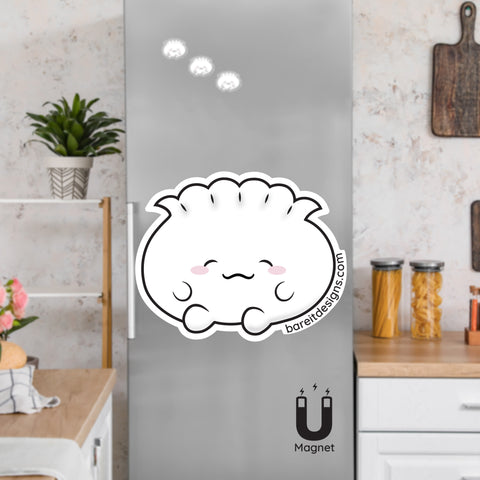 Product picture of a cute flexible dumpling fridge magnet with a background example of dumpling magnets clinging to a stainless steel fridge. Dumpling magnet is designed by Bare It Designs.
