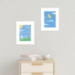 Flying A Cat First and Second Half (set of two) art prints by Bare It Designs, Edmonton, AB, Canada. A white cat is shown holding a kite string that is attached to an orange cat on another art print and the cat is flying in the air like a kite on a beautiful summer sunny day with blue skies.