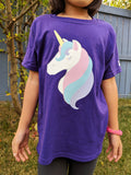 Model is wearing a youth small purple tshirt with a glittery unicorn head with pastel purple, pink, and blue mane and eyelashes. Designed and printed by Bare It Designs.